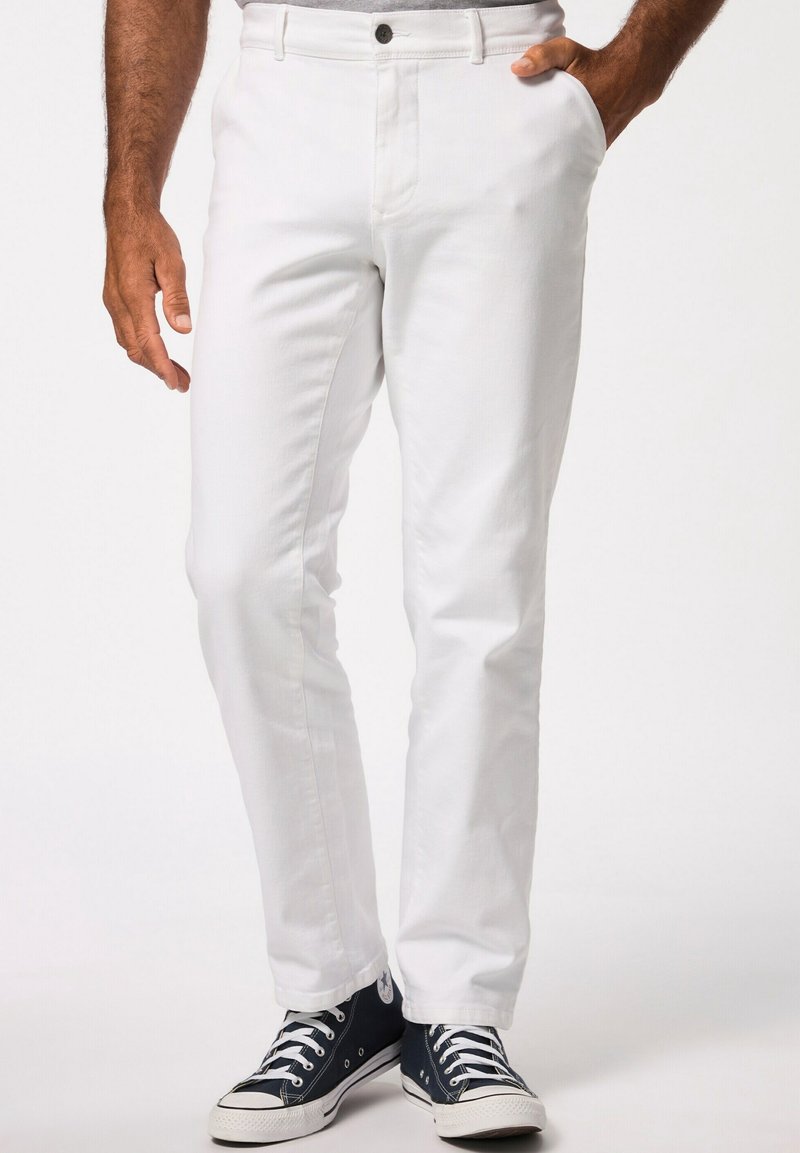 Pantaloni bianchi in cotone dal taglio slim, con passanti per cintura e chiusura con bottone anteriore. Indossati con sneakers in tela blu con dettagli bianchi.