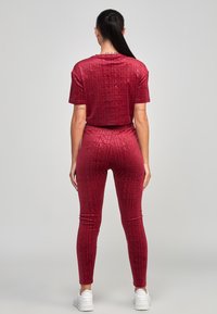 Conjunto burdeos de tela suave con un patrón de logotipos en toda la prenda, mangas cortas y pantalones ajustados. Combinado con zapatillas blancas.