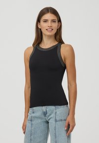 Czarny bezrękawnik z elastycznego materiału, z fakturowanym dekoltem i metalicznymi akcentami. W połączeniu z jasnoniebieskimi dżinsami.