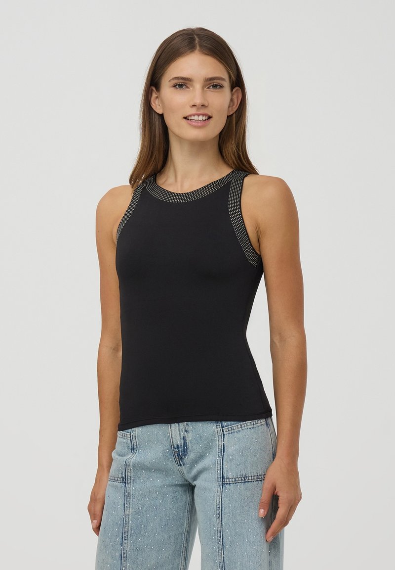 Czarny bezrękawnik z elastycznego materiału, z fakturowanym dekoltem i metalicznymi akcentami. W połączeniu z jasnoniebieskimi dżinsami.