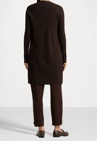 Lungo maglione tunica marrone a coste con silhouette dritta, abbinato a pantaloni marroni coordinati con dettagli a bottoni ai polsini.