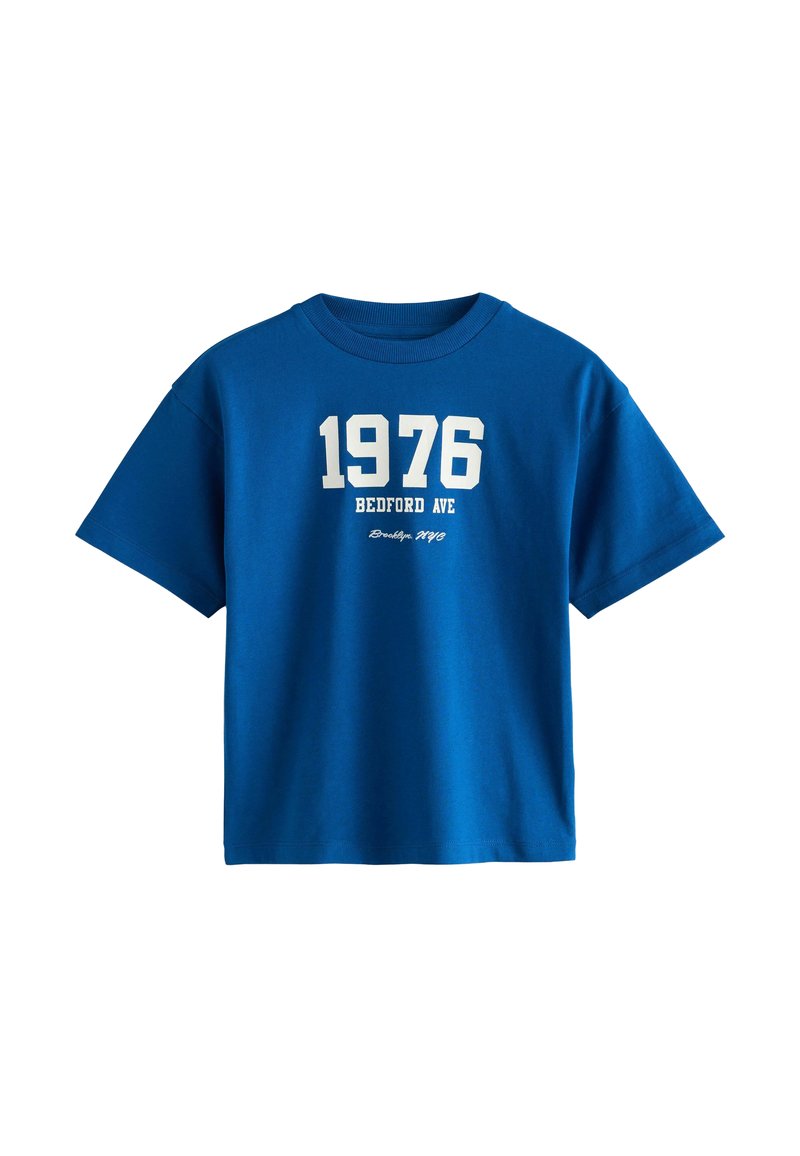 Zila kokvilnas T-kreklis ar apaļu kaklu. Priekšējā grafika ietver "1976" un "BEDFORD AVE" baltā krāsā, ar "Brooklyn, NYC" mazākā tekstā.