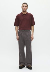 Μπορντό μπλουζάκι πόλο με κοντά μανίκια και υφή, σε συνδυασμό με φαρδιά γκρι παντελόνια και μαύρα δετά παπούτσια. Απλή, άνετη γραμμή.