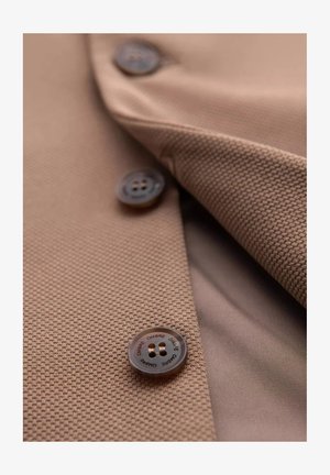 Veste marron en tissu texturé, avec des boutons marron lisses et un éclat subtil. Le col et le revers sont visibles en gros plan.