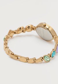 Ρολόι βραχιόλι σε χρυσό τόνο με πολύχρωμους πολύτιμους λίθους και πίσω μέρος από ατσάλι με χαραγμένη την επωνυμία Swarovski.