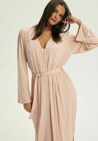 Długa różowa sukienka wrap z miękkiego materiału, z szerokimi rękawami, wiązanym stanem i głębokim dekoltem w kształcie litery V.