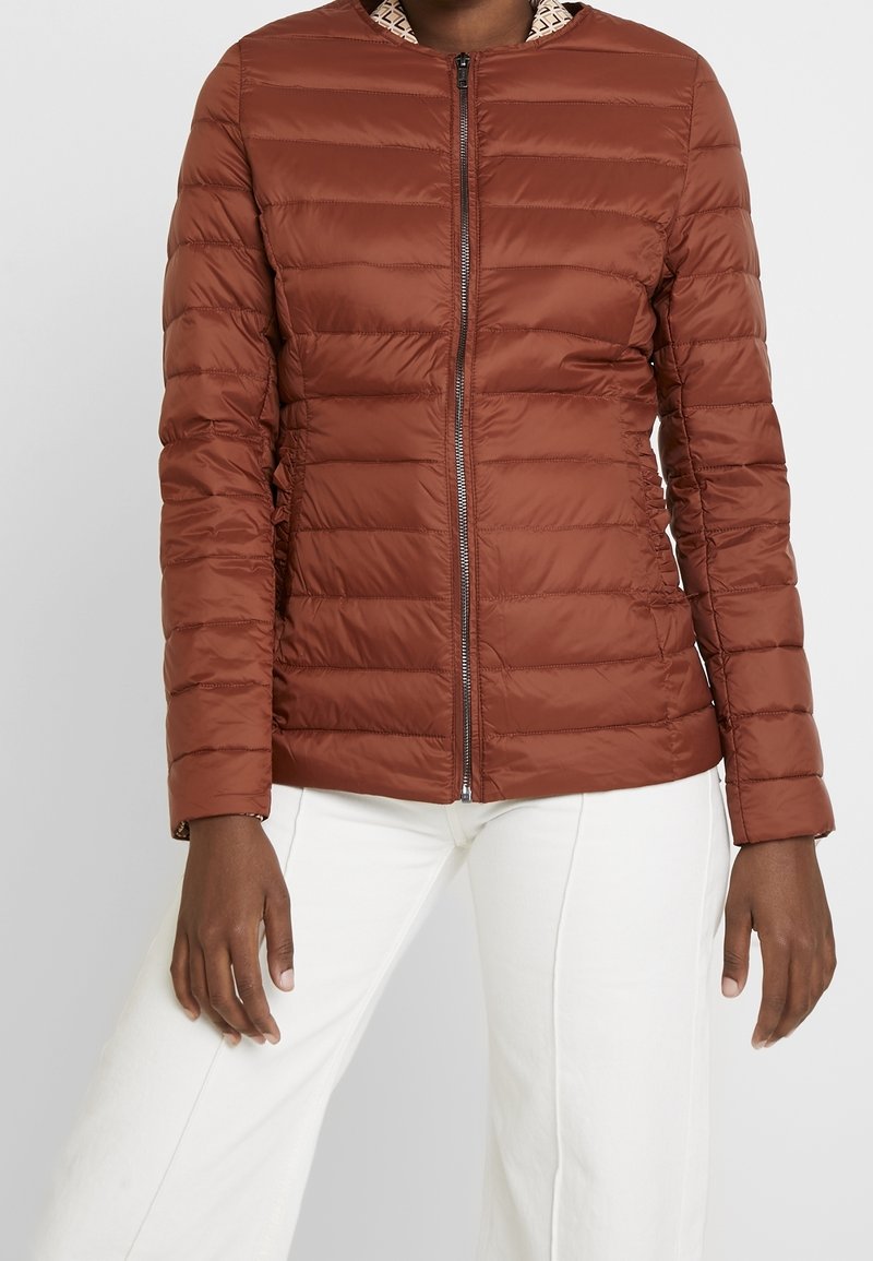 Brown puffer jacket with horizontal stitching and a zip closure. Features a patterned inner collar. Worn with white flared pants.