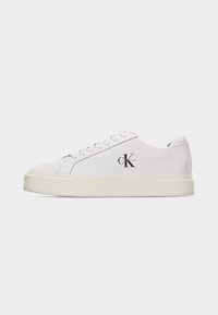 Λευκό sneaker Calvin Klein χαμηλού ύψους με δέσιμο κορδονιών και μπεζ χοντρή σόλα, λογότυπο CK στο πλάι, εμφανιζόμενο προφίλ σε λευκό φόντο.