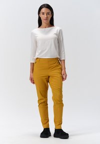 Gula byxor med slim fit, med sidofickor. Matchas med en vit långärmad topp med rund halsringning. Svarta skor fulländar outfiten.