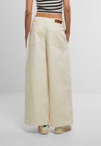 Cream wide-leg pants with patch pockets and a leather label on the waistband, paired with light-colored shoes. Striped crop top visible.