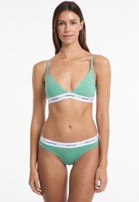 Grünes Baumwoll-Bralette und Bikini-Set mit V-Ausschnitt, dünnen Trägern und weißen elastischen Bändern mit "GUESS JEANS"-Branding.