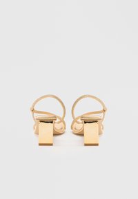 Gold heeled sandals with textured straps and a square block heel. Features a delicate, shimmering ankle strap for secure fastening.