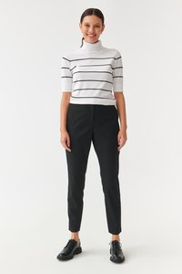 White striped turtleneck top with black lines, paired with black tapered pants and black lace-up shoes. Smooth textures throughout.