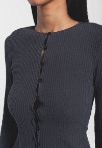 Navy ribbed sweater with long sleeves, featuring a round neckline and a placket of black buttons down the front. Textured knit design.