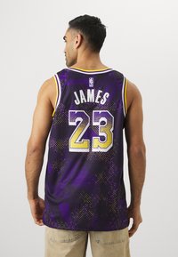 Canotta da basket viola con un design grafico, caratterizzata da accenti gialli, numero "23" e nome "JAMES" sul retro. Realizzata in tessuto traspirante.