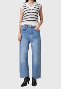 Hvid og sort stribet strikvest med V-hals, parret med høj talje blå brede jeans og sorte hælede ankelstøvler.