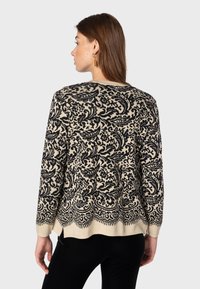 Beige tröja med ett detaljerat svart paisleymönster, rundad halsringning och ribbade ärmslut. Avslappnad passform med sidospår i fållen.