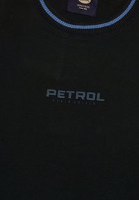 Camiseta de algodón negra con cuello redondo, que presenta un ribete azul. El texto en el frente dice "PETROL D.E.N.I.M. DRIVEN" en un azul claro que contrasta.