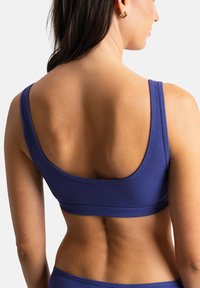 Bralette violet à côtes avec un style bandeau large. Présente des bretelles épaisses et une finition lisse. Design minimaliste sans matériel visible.