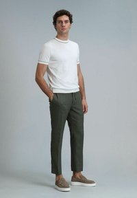 Weißes T-Shirt mit kurzen Ärmeln und schwarzem Rand, kombiniert mit olivgrünen, schmal zulaufenden Hosen und hellbraunen Slippern mit weißen Sohlen.