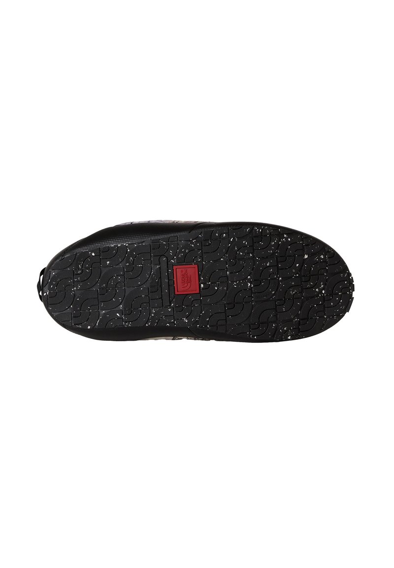 Svart skosula med ett mönster, vita fläckar och en röd fyrkantig logotyppatch i mitten.