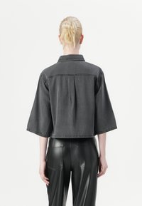Gray denim cropped jacket with wide sleeves, a back pleat, and a pointed collar, paired with high-waisted black leather pants.
