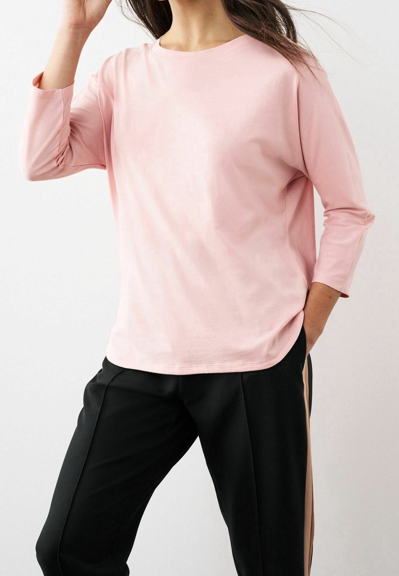 Top de manga larga rosa claro, hecho de una tela suave, con escote redondo y corte holgado, combinado con pantalones negros que presentan rayas laterales.