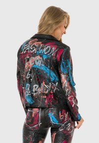 Black leather jacket with colorful, abstract paint splatters. Features white painted text and a fitted design, accompanied by matching pants.