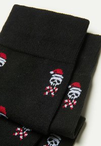 Black socks made of knitted fabric featuring a pattern of white skulls with red Santa hats and candy canes. Soft texture with ribbed cuffs.