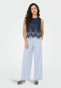 Top senza maniche blu navy con motivo floreale ricamato; pantaloni a gamba larga azzurri; tacchi neri con dettagli floreali.