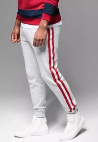 Graue Sweatpants mit roten Streifen an den Seiten, im taillierten Schnitt und mit elastischen Bündchen. Kombiniert mit weißen High-Top-Sneakern.
