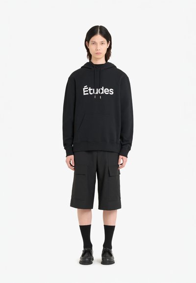 Sweat à capuche noir avec le logo "Études", associé à un short cargo noir, des chaussettes noires et des chaussures noires. Design simple et décontracté.