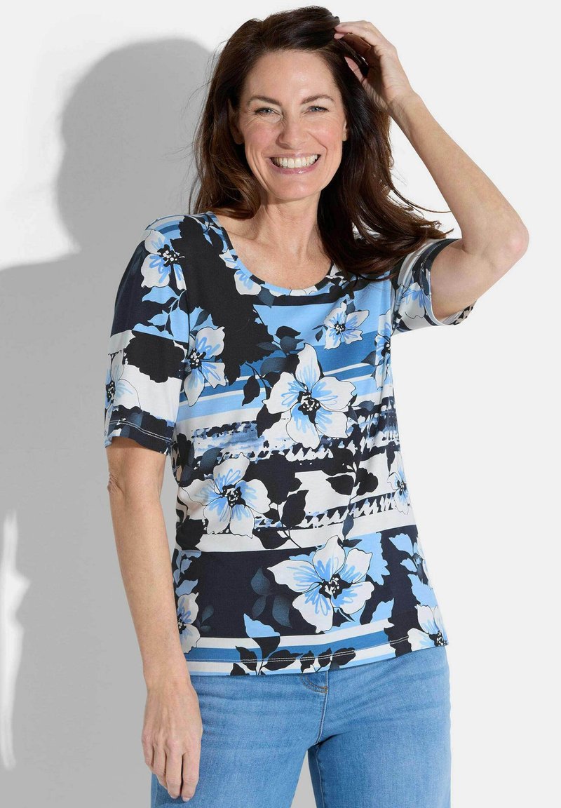 Bloemig top met korte mouwen en een ronde hals. Heeft blauwe en zwarte bloemenpatronen op een lichtblauwe achtergrond. Zachte, gladde stof.