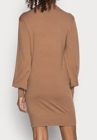 Robe pull en tricot marron avec de longues manches bouffantes, des poignets et un ourlet côtelés. Texture douce et design ajusté, s'étendant au-dessus de la mi-cuisse.