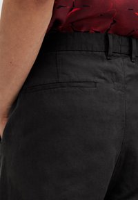 Black linen trousers featuring a smooth texture, slim fit, belt loops, and a single back pocket with a subtle seam detail.