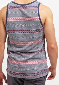 Débardeur gris avec des rayures horizontales aux motifs géométriques rouges et bleu marine. Tissu doux avec un col rond et un design sans manches.