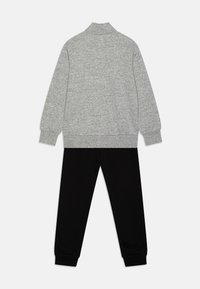 Sudadera gris con cuello alto, combinada con pantalones de chándal negros. Ambos están hechos de una tela suave, presentan puños elásticos y un ajuste relajado.