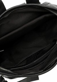 Innenansicht einer schwarzen Lederhandtasche mit glatter Textur, ausgestattet mit einem Reißverschlussfach und einem Stofffutter. Einfaches Design mit mehreren Taschen.