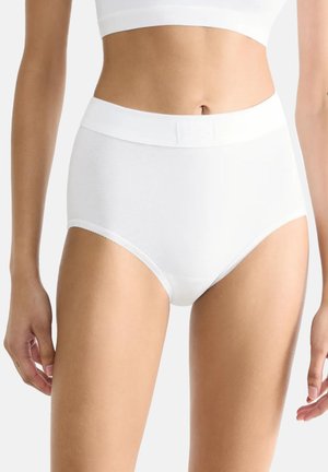 Kvinde iført hvide seamless trusser med høj talje og en hvid crop top, vist fra midt på torsoen til det øverste af lårene.