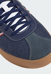 Navy and gray sneaker with denim and suede materials, rubber sole, white laces, and contrasting red and white stripes along the side.
