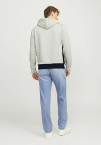 Sudadera gris con capucha, dobladillo y puños en contraste azul marino. Combinada con jeans azul claros y zapatillas blancas, vista desde la parte trasera.