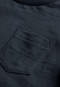 Dunkelgraues T-Shirt aus strukturiertem Stoff, mit einer kleinen Brusttasche. Der Rundhalsausschnitt hat eine glatte Verarbeitung.