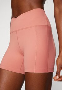 Růžové aktivní šortky s vysokým pasem, vyrobené z hladké, elastické tkaniny. Mají detaily švů a přiléhavý design.