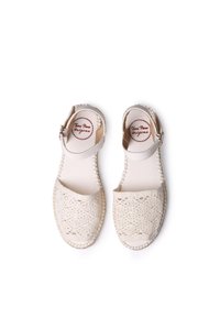 Light beige sandals with lace-like cutouts, adjustable ankle strap, and a woven edge. Soft material, flat sole, and fabric insole.