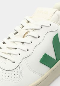 Sapatilhas de couro branco com o logotipo "V" verde, painéis de atacadores texturizados, biqueira perfurada e língua de cor creme.