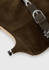 Stivaletto in suede marrone con cerniera metallica e dettagli con fibbia. Presenta una punta appuntita e un accento argento sul tacco.