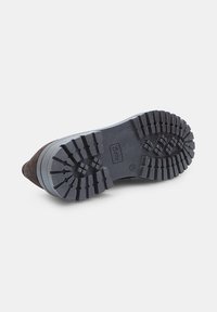 Suola di scarpa in gomma nera con profondi motivi di battistrada e un design curvo. Punta affusolata con dettagli in suede di colore marrone scuro.
