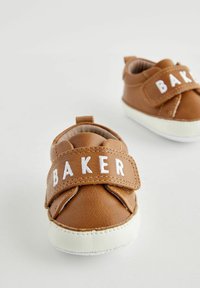 Sneakers in finta pelle marrone con suola in gomma bianca, dotate di una prominente fascia in velcro con la scritta "BAKER" in bianco. Design morbido e arrotondato.