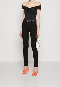 Černý body s odhalenými rameny a řasenými detaily, doplněný o černé džíny s vysokým pasem, jasně oranžov é vysoké podpatky a bílou kabelku.