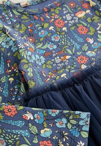 Tissu bleu à texture côtelée présentant un motif coloré floral et champignon à côté d'un tulle foncé froncé.